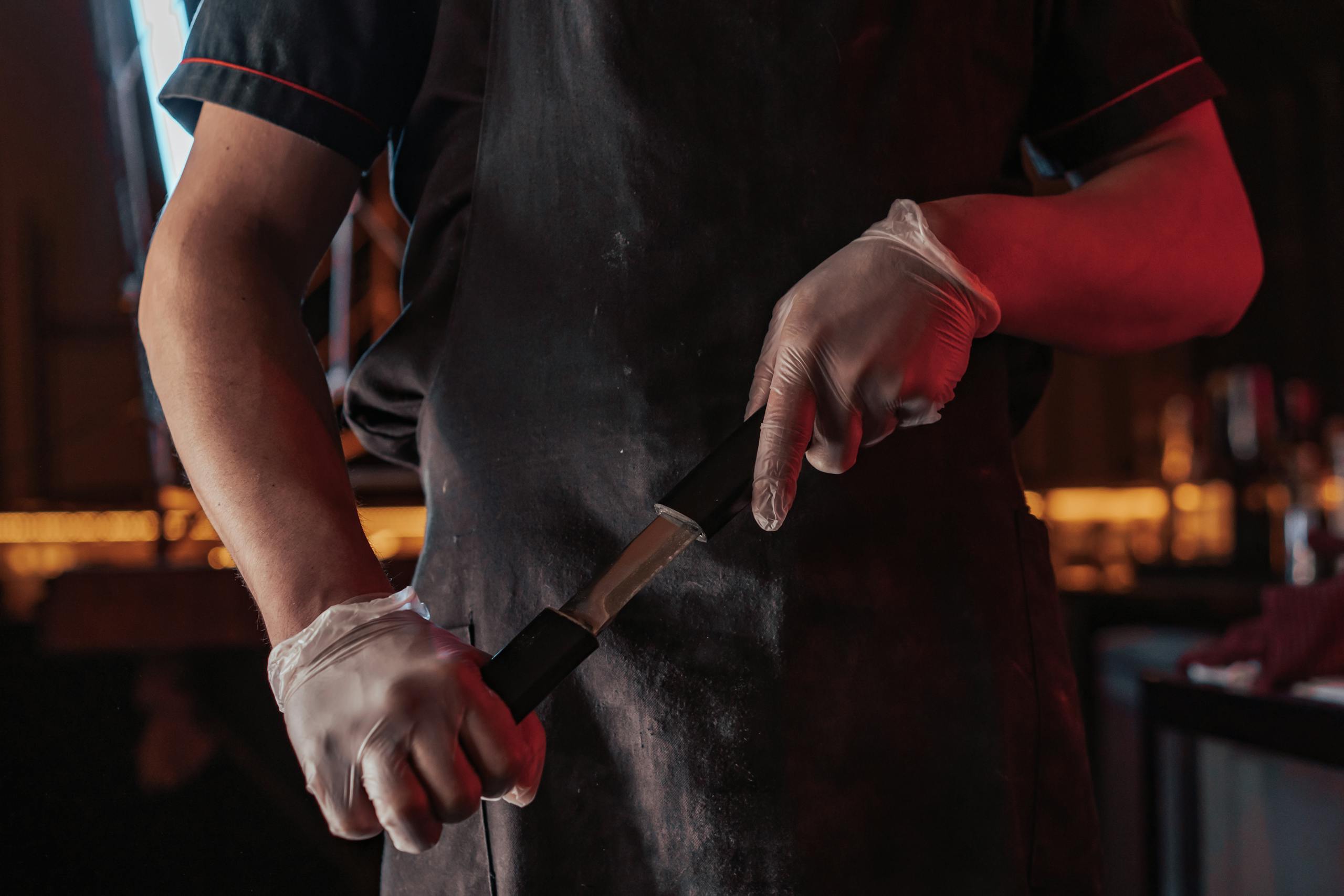Chef sharpening a knife wearing gloves in a dimly lit kitchen, enhancing precision.